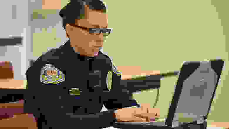 Police officer works on her laptop computer in a classroom.